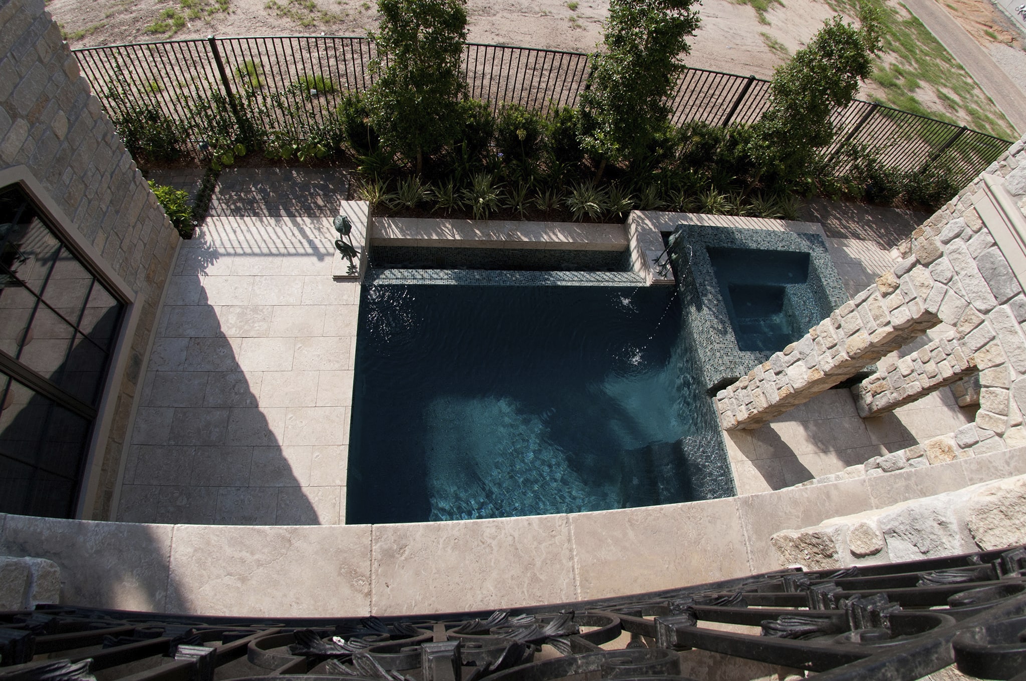 View from above of a compact East Shore pool, raised spa, patio, and adjacent home designed by Texas Pools