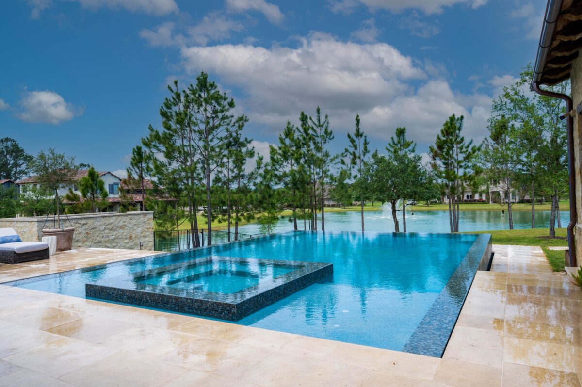 Custom pool with a raised square spa and stone decking overlooking a lake, built by Texas Pools.