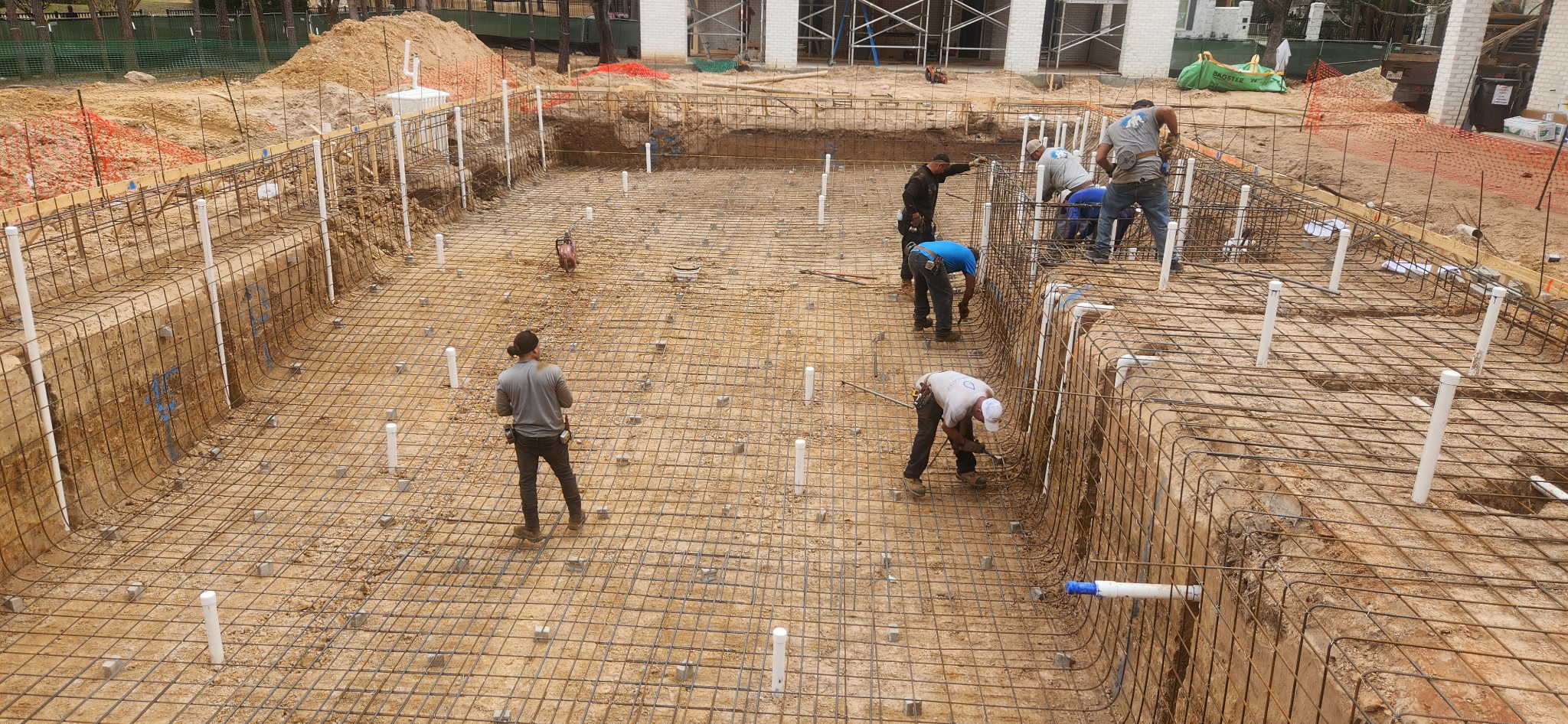 Crew working on steel reinforcement across the excavated pool floor, walls, and raised sections before gunite application.